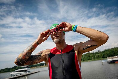 SwimRun Rheinsberg 2022: Male participant puts on sunglasses, the lake behind him