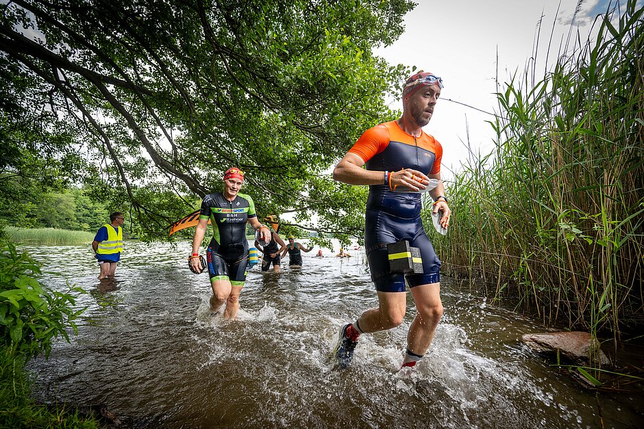 SwimmRun 2023: Läufer durchqueren das seichte Wasser der Uferböschung © SCC EVENTS / Tilo Wiedensohler