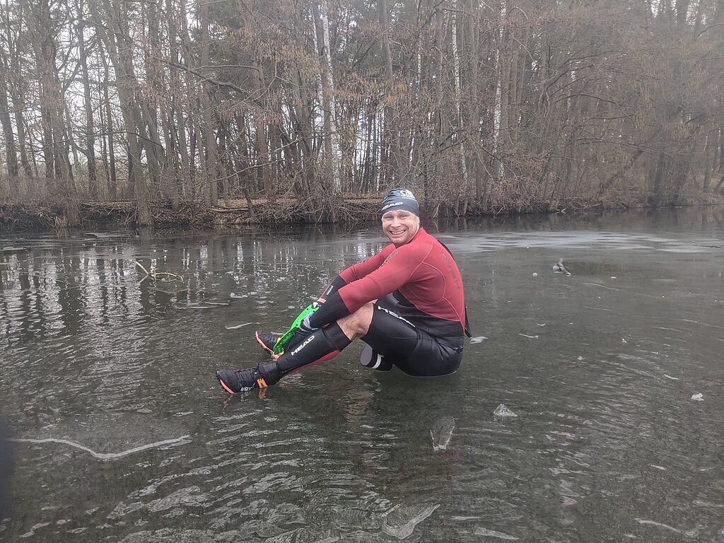 SwimRun: Male swimmer sits on a sheet of ice surrounded by forest © SCC EVENTS / privat